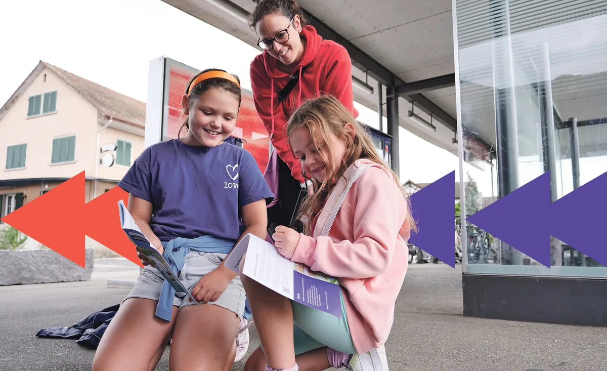 Zwei Kinder knien am Boden und schreiben etwas in eine Broschüre. Ihre Mutter blickt ihnen über die Schulter.